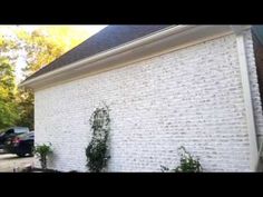 a white brick building with plants growing on the side and cars parked in the driveway