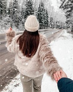 a person holding the hand of another persons hand on a snowy road with trees in the background