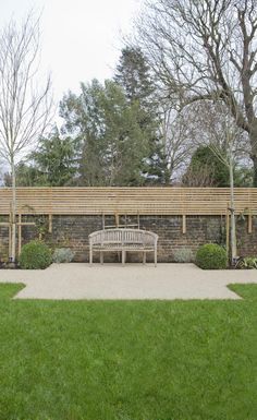 a wooden bench sitting in the middle of a lush green park next to a brick wall