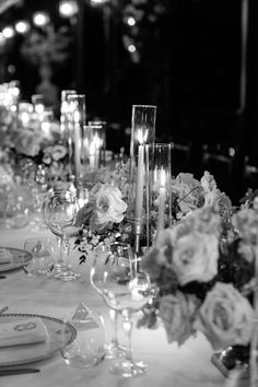 black and white photograph of table setting with candles, flowers and plates on it at night