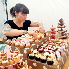 a woman standing in front of a table filled with cupcakes