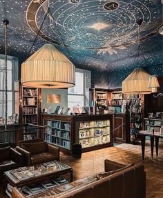 a library with many books on shelves and lamps hanging from the ceiling over it's seating area