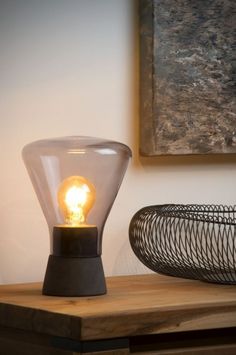 a light bulb sitting on top of a wooden table next to a basket and painting