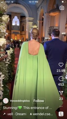 the back of a woman in a green dress walking down a red carpeted hall