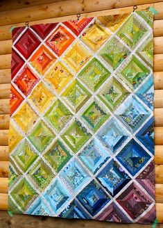 a multicolored quilt hanging on the side of a wooden wall in front of a log cabin