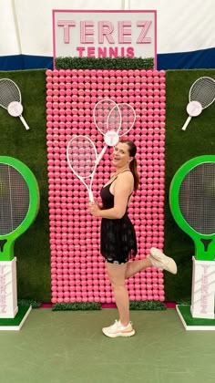 a woman holding two tennis racquets standing in front of a wall made out of tennis balls