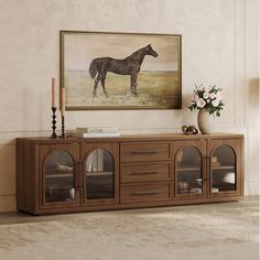 a horse painting hanging on the wall above a wooden entertainment center with glass doors and drawers