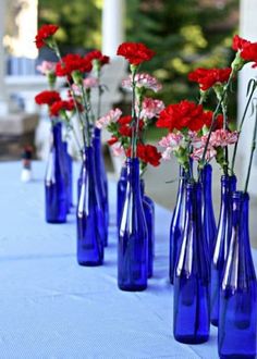 several blue vases with red and white flowers in them sitting on a table outside