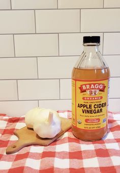 a bottle of apple cider vinegar next to an onion on a wooden cutting board