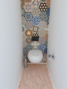 a white toilet sitting inside of a bathroom next to a wall covered in colorful tiles