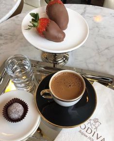 two chocolate covered strawberries on top of a plate next to a cup of coffee