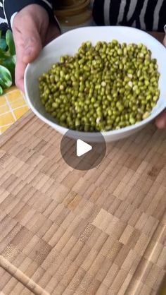 a person holding a white bowl filled with green beans on top of a wooden cutting board