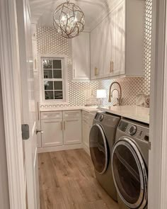 a washer and dryer in a small room with white cabinets, wood flooring and a chandelier hanging from the ceiling