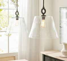 two glass lamps hanging from a ceiling in a room with white curtains and windows behind them