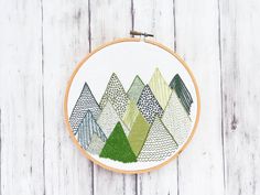 a cross stitch pattern in the shape of trees on a white wood background with a wooden hoop