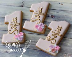 three decorated cookies with pink and gold frosting are on a wooden table next to each other