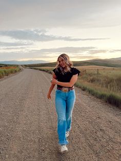 a woman walking down the middle of a dirt road