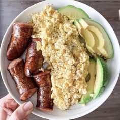 a white plate topped with meat and veggies next to an avocado