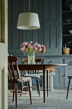 a dining room table and chairs with flowers in a vase on the table next to it