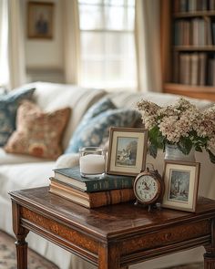 a coffee table with books, candles and flowers on it in front of a couch