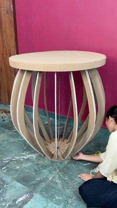 a woman sitting on the ground next to a wooden table with curved legs and circular top