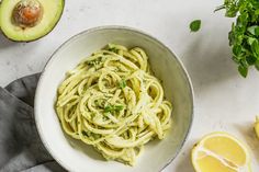 a white bowl filled with pasta next to sliced lemons and an avocado