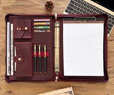 an open leather case with writing utensils and notebooks in it on a wooden table