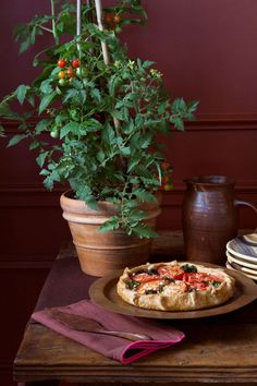 a pizza sitting on top of a wooden table next to a potted plant