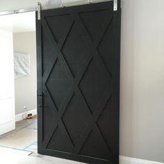 a black sliding door in the middle of a room with white walls and blue tape on the floor