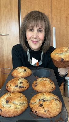 a woman holding up some muffins in front of her face on a tray