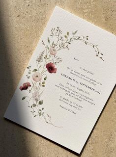 a wedding card with watercolor flowers and leaves on the front, sitting on a table