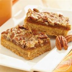 three pieces of pecan bars on a plate with some nuts next to it and a glass of orange juice in the background