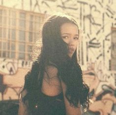 a woman with long hair standing in front of graffiti