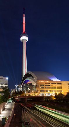 a train passing by a tall building with a spire in the background at night time