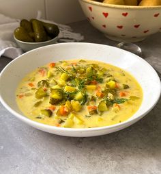 a white bowl filled with soup next to two bowls of olives and pickles