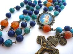 Absolutely gorgeous "Flame of Love" rosary made with 8mm light blue jade, 8mm dyed lapis and 10mm fire agate, adorned with filigree caps and daisy spacers. Ornate oval medallion with the image of Our Lady Flame of Love. Pardon crucifix and a St. Benedict charm to complete the piece.  Along with your rosary you will receive a prayer card with the Litany of Our Lady and an organza bag for your new sacramental. Medallion 1 1/8 x 1 3/8-inch; Pardon Crucifix 2 x 1 2/8 inch; 22-inch total rosary lengt Blue Rosary With 8mm Beads For Healing, Blue Spiritual Rosary With Gemstone Beads, Spiritual Blue Rosary With Gemstone Beads, Blue Gemstone Beads Rosary For Spiritual Use, Blue Spiritual Rosary Bracelet With 8mm Beads, Flame Of Love, Fancy Ribbon, Blue Jade, St Benedict