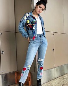 a woman standing in front of a wall wearing ripped jeans and a denim jacket with patches on it