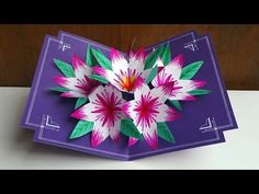 an origami flower is placed on top of a purple card with white and pink flowers