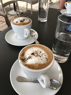 two cups of cappuccino on a table with spoons and water glasses