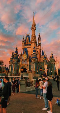 people are standing in front of a castle at dusk with the sky painted pink and blue