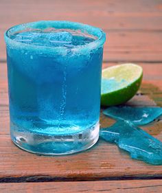 a blue drink sitting on top of a wooden table next to a slice of lime