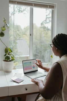 a woman sitting at a desk with a laptop computer on her lap looking out the window