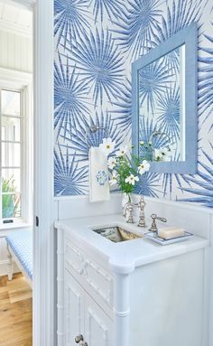 a white sink sitting under a mirror next to a blue and white wallpapered bathroom