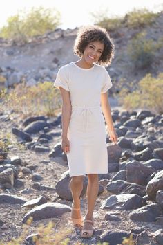 a woman in a white dress is standing on some rocks and smiling at the camera