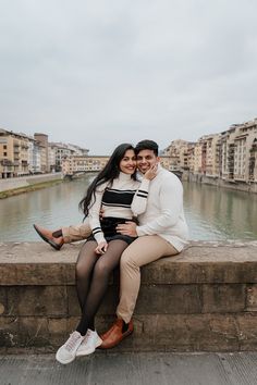 a man and woman sitting next to each other on a stone wall near the water