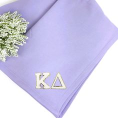 a lavender colored napkin with the letters k and a small white flower on top of it