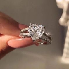 a woman's hand holding an engagement ring with a heart shaped diamond on it