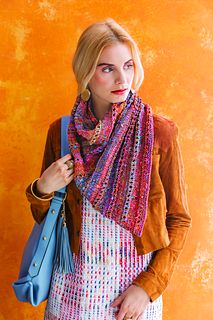 a woman holding a blue purse and wearing a colorful scarf over her shoulders, standing in front of an orange wall