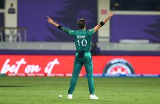 a man standing on top of a green field holding his arms up in the air