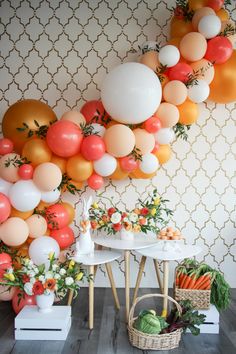 an assortment of fruits and vegetables are displayed in front of a wall with balloon garlands